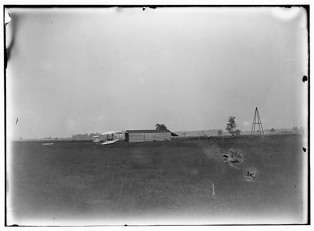 [Start of the first flight of 1905, Orville Wright at controls of the machine, near the hangar at Huffman Prairie. The two figures in the center are probably Wilbur Wright and Charles E. Taylor. The catapult launching device appears for the first time in a photograph]