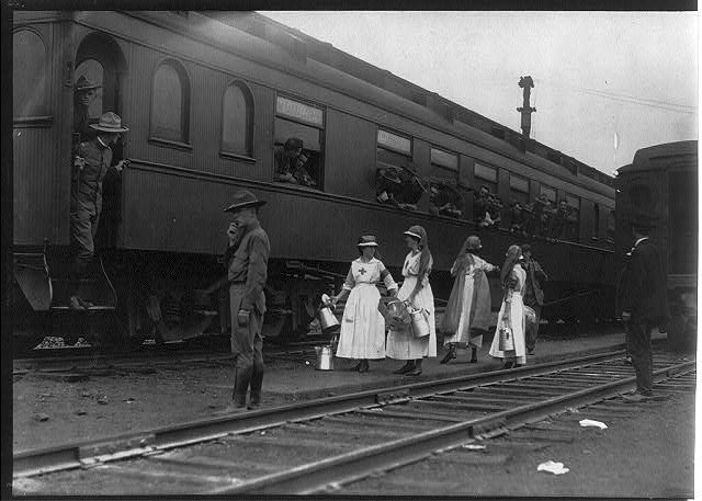 Men on troops train, with Red Cross workers in front, probably in Washington, D.C.