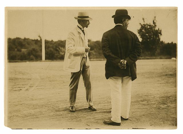 [Two men, probably journalists, standing on a field]