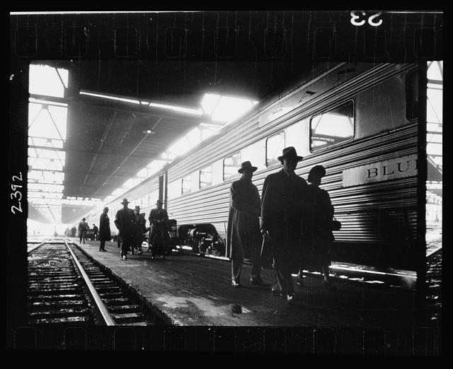 [Men, probably commuters, walking along a platform next to a train]