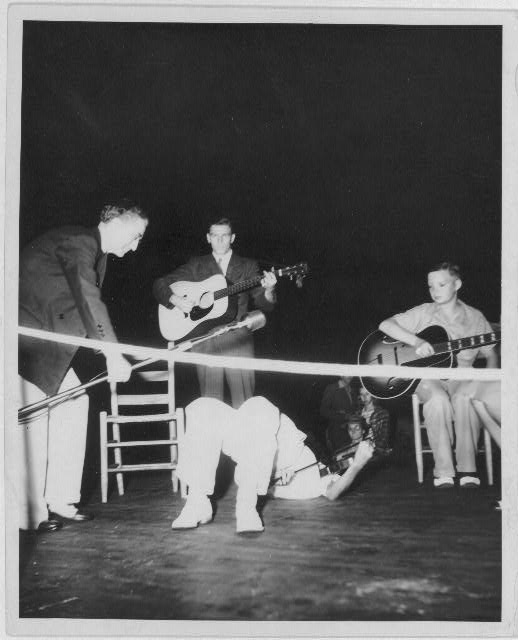 [Sunny Side Boys, two youngsters, one of whom is on his back playing the fiddle, with an older man playing guitar. Bascom Lamar Lunsford is probably the man to the right of the picture holding a microphone above the fiddler]