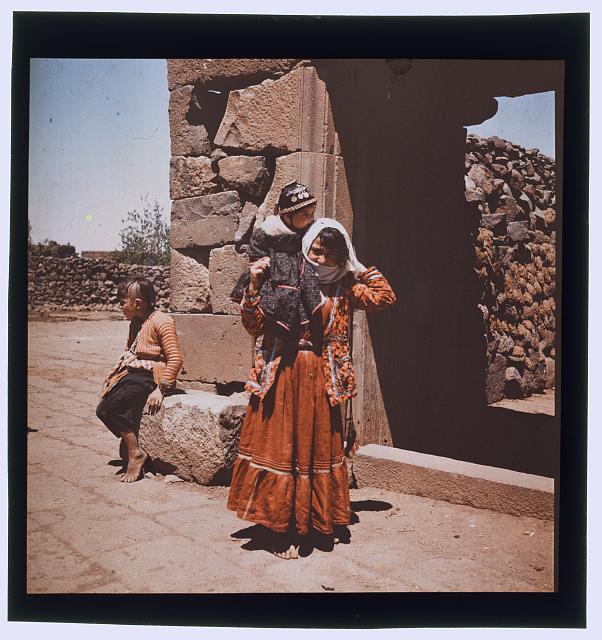 [Girl holding baby near ruins, probably in Syria]