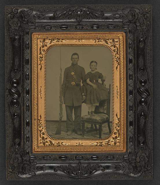 [Unidentified young soldier in Union frock coat with bayoneted musket next to unidentified young girl standing on chair; probably siblings]