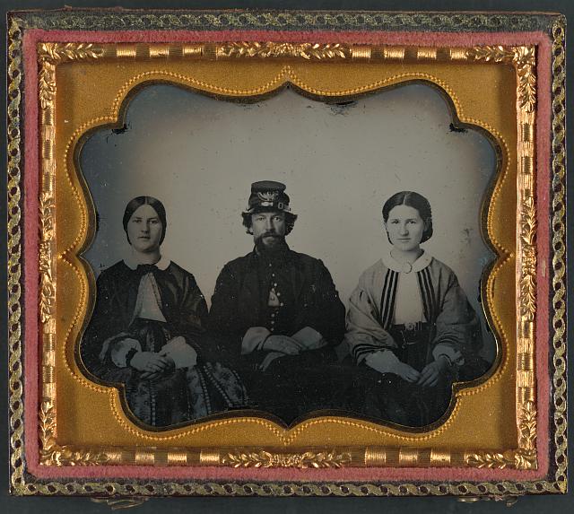 [Unidentified soldier in infantry uniform sitting between two women, probably relatives]