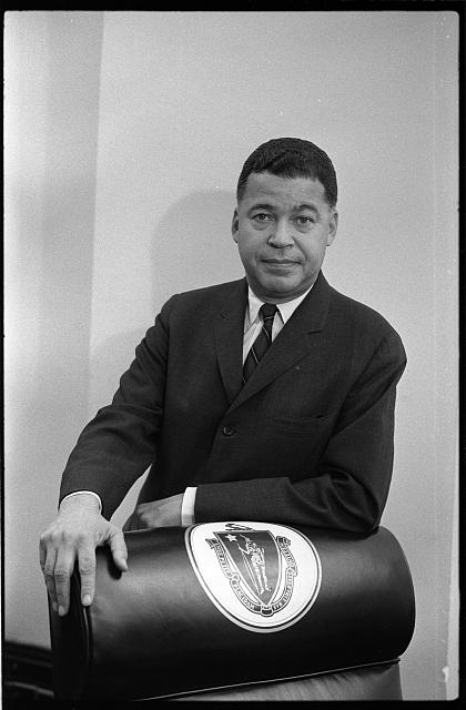 [Senator Edward Brooke standing behind a chair which is decorated with the Great Seal of the Commonwealth of Massachusetts, probably in Washington, D.C. after his election]