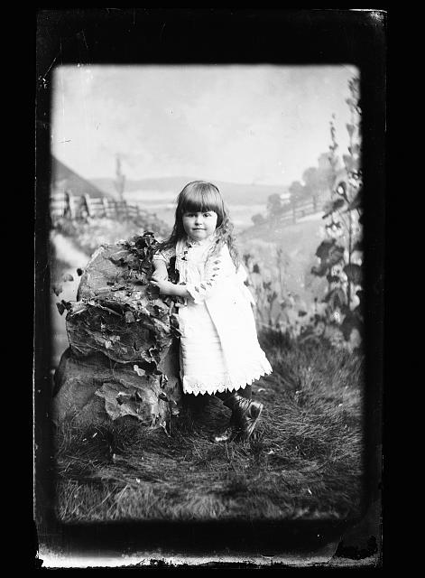 [Girl, probably Hallie Jackson, in white dress posed against rock in studio background]