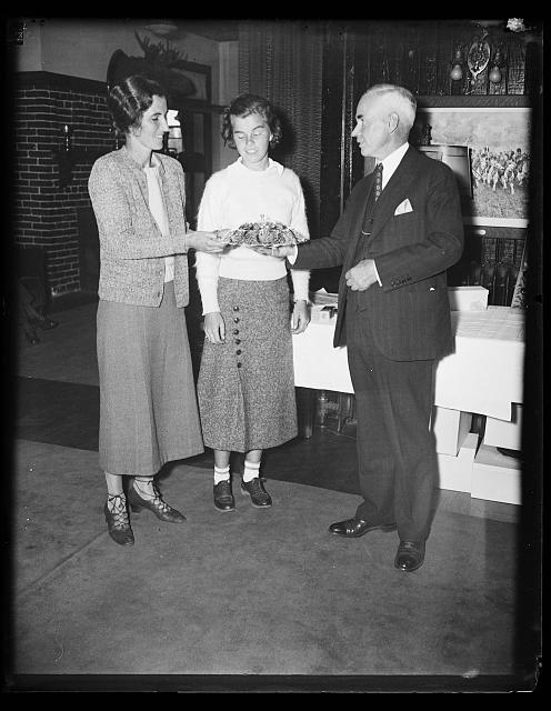 [Two women, possibly Marian McDougall, an amateur golf champion, center; and man, probably at a sports/golf club (golf balls are on the table)]