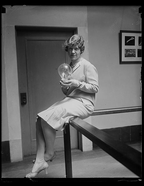 [Woman holding object, probably a light bulb]
