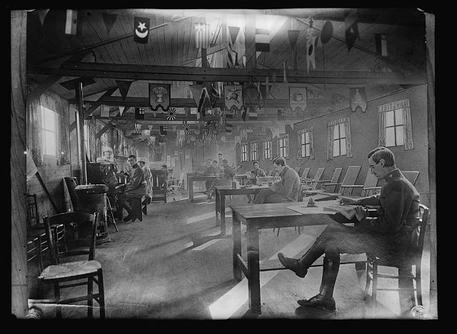Officers' sitting room in the American Red Cross recreation hut ar Orly, France. This is probably one of the coziest rooms of its kind in France. The decorations were arranged by the Red Cross girls in charge, and with streamers and banners of the ceiling, tasty hangings at the windows and gay posters on the walls make this a most attractive place in which to while away any spare moments which the officers may have