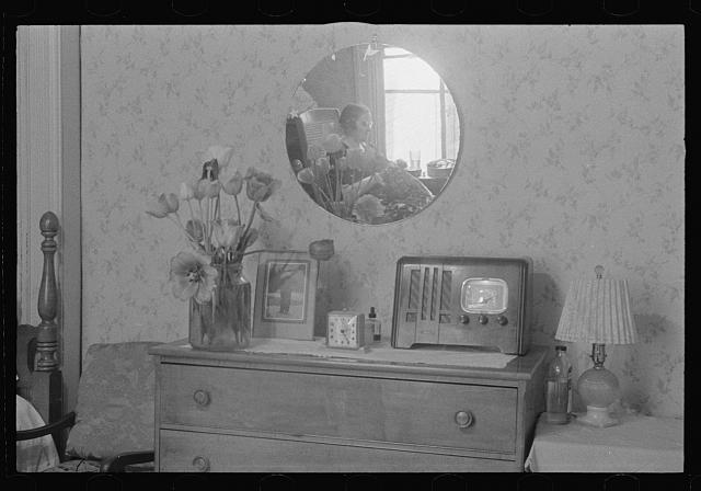 Washington, D.C. A corner of a bedroom, probably in a rooming house for government clerks, showing reflected in a round mirror above a dresser a woman doing handwork