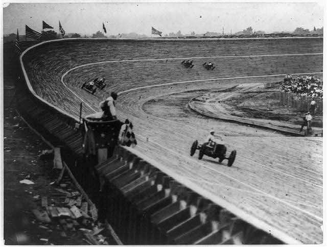 [Automobile racing on curved wood track, probably in or near Washington, D.C., with flag man in foreground]