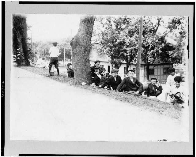 [Group of boys with golf clubs--probably caddies--resting on hill]