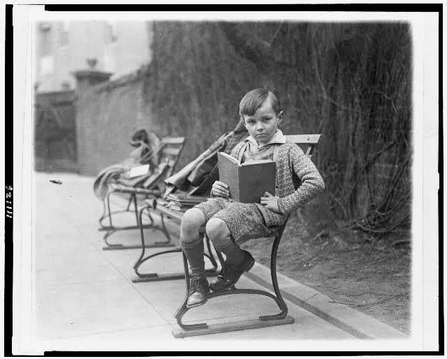 [Unidentified boy, seated on park bench, probably in Washington, D.C., holding book]