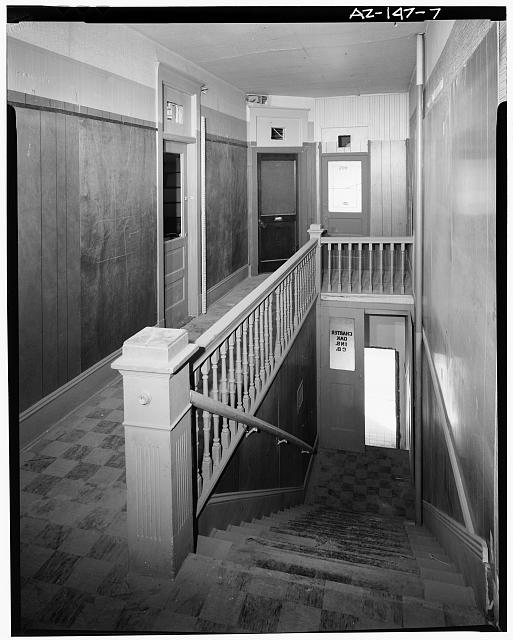 7.  View (looking west) of the second floor corridor in the south segment of building. The second floor was designed for residential rental rooms. The guardrail, balusters, newel posts, and handrail, as well as the two upper-level door openings with transoms, are original features. The doors, proper, are nonoriginal and probably were installed when the second floor was converted to office use. The pair of doors (one leaf is open and one is closed) is located at the intermediate stair landing. The original exterior doorway (without a door) is located at the bottom of the stair. The upper-level door without a transom is nonoriginal, as are the floor tile and wall paneling. At the time of documentation a suspended ceiling and duct were removed to ... - Stroud Building, 31-33 North Central Avenue, Phoenix, Maricopa County, AZ