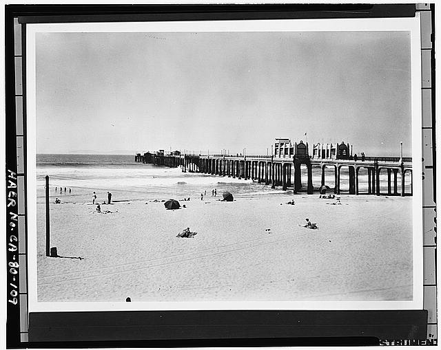 109.  VIEW OF SOUTHEAST SIDE OF PIER TAKEN FROM BEACH, LOOKING WEST. VIEW SHOWS ART DECO BUILDINGS ADDED IN 1931 AND 5TH TEE ADDED IN 1940 Photograph #5369-HB. Photographer unknown, c. 1945, based on clothing of sunbathers; view probably taken in mid-1945 after the U.S. Army vacated the pier and it was reopened to the public. - Huntington Beach Municipal Pier, Pacific Coast Highway at Main Street, Huntington Beach, Orange County, CA