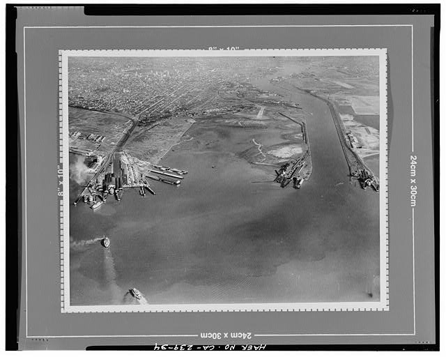34.  LOW OBLIQUE AERIAL VIEW LOOKING EAST OVER THE FUTURE SITE OF THE NAVAL SUPPLY CENTER TO DOWNTOWN OAKLAND. THE FEDERAL CHANNEL IS AT THE RIGHT. No date, probably mid 1930's.  Clyde Sunderland, photographer. Original print on file at the Port of Oakland, California. - Oakland Harbor Training Walls, Mouth of Federal Channel to Inner Harbor, Oakland, Alameda County, CA