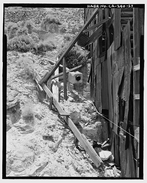 27.  DETAIL OF PROBABLY LOCATION OF PELTON WATER WHEEL ON EAST SIDE OF MILL, LOOKING SOUTH SOUTHWEST. THE END OF THE WATER PIPELINE ENCASED IN A SQUARE BLOCK OF CONCRETE IS AT CENTER. THIS IS THE END OF A 23-MILE PIPELINE THAT SUPPLIED WATER FROM TELESCOPE PEAK IN THE PANAMINT MOUNTAINS. - Skidoo Mine, Park Route 38 (Skidoo Road), Death Valley Junction, Inyo County, CA