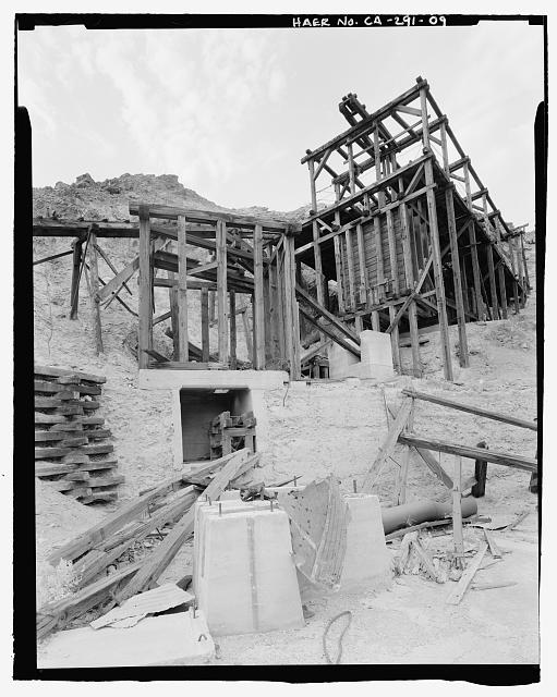 DETAIL VIEW OF LOWER TRAM TERMINAL, SECONDARY ORE BIN, CRUSHER FOUNDATION, AND BALL MILL FOUNDATIONS, LOOKING NORTH NORTHWEST. ORE FROM THE MINES WAS DUMPED FROM THE TRAM BUCKETS INTO THE PRIMARY ORE BIN UNDER THE TRAM TERMINAL. A SLIDING CONTROL DOOR INTRODUCED THE INTO THE JAW CRUSHER (FOUNDATIONS,CENTER). THE CRUSHED ORE WAS THEN CONVEYED INTO THE SECONDARY ORE BIN AT CENTER LEFT. A HOLE IN THE FLOOR OF THE ORE BIN PASSED ORE ONTO ANOTHER CONVEYOR THAT BROUGHT IT OUT TO THE BALL MILL(FOUNDATIONS,CENTER BOTTOM). THIS SYSTEM IS MOST LIKELY NOT THE ORIGINAL SET UP, PROBABLY INSTALLED IN THE MINE'S LAST OCCUPATION IN THE EARLY 1940s.  - Keane Wonder Mine, Park Route 4 (Daylight Pass Cutoff), Death Valley Junction, Inyo County, CA