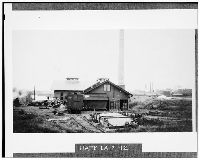12.  (Credit CBF) West end of McNeil Street Station in November 1911. The settling basins are visible on the far right. In the foreground is a pile of filter sand and several barrels of chemicals (probably lime or alum). The box car is delivering chemicals to storage in the west wing of the station.  - McNeil Street Pumping Station, McNeil Street & Cross Bayou, Shreveport, Caddo Parish, LA