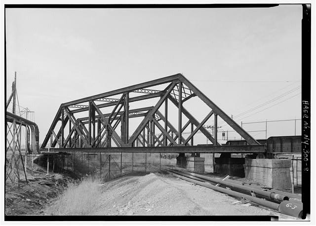 TWIN SKEWED TRUSS RAILROAD BRIDGES NEAR BRIDGE STREET AT THE WEST END OF THE PLANT.  THIS VIEW PROBABLY LOOKING NORTHWEST.  BRIDGES BUILT OVER ERIE CANAL (WHICH FLOWED RIGHT THROUGH THE MIDDLE OF THE PLANT) BY AMERICAN BRIDGE COMPANY IN 1902.  SINCE THIS PHOTO WAS TAKEN, NEAR BRIDGE HAS BEEN DEMOLISHED; FAR BRIDGE IS STILL IN SERVICE. - Solvay Process Company, Between Willis & Milton Avenues, Solvay, Onondaga County, NY