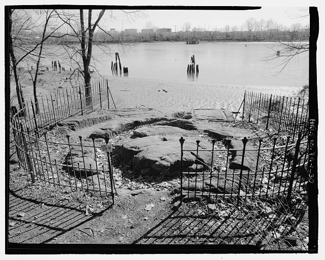 CIDER PRESS, LOOKING SOUTHEAST ACROSS THE SCHUYLKILL RIVER. THIS PRESS, CARVED OUT OF A LARGE BOULDER AT THE RIVERS EDGE, PROBABLY DATES FROM THE LIFETIME OF JOHN BARTRAM, IF NOT TO THE SWEDISH SETTLERS BEFORE HIM. THE IRON FENCE IS A NINETEENTH-CENTURY ADDITION - John Bartram House & Garden, 54th Street & Lindbergh Boulevard, Philadelphia, Philadelphia County, PA